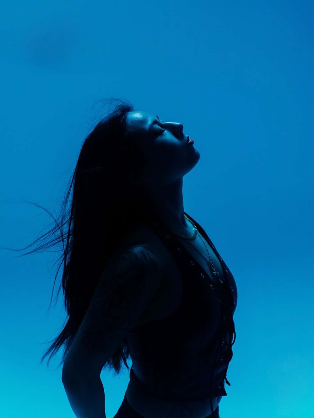 LilyannaMarie in silhouette against a blue backdrop, head tilted back.