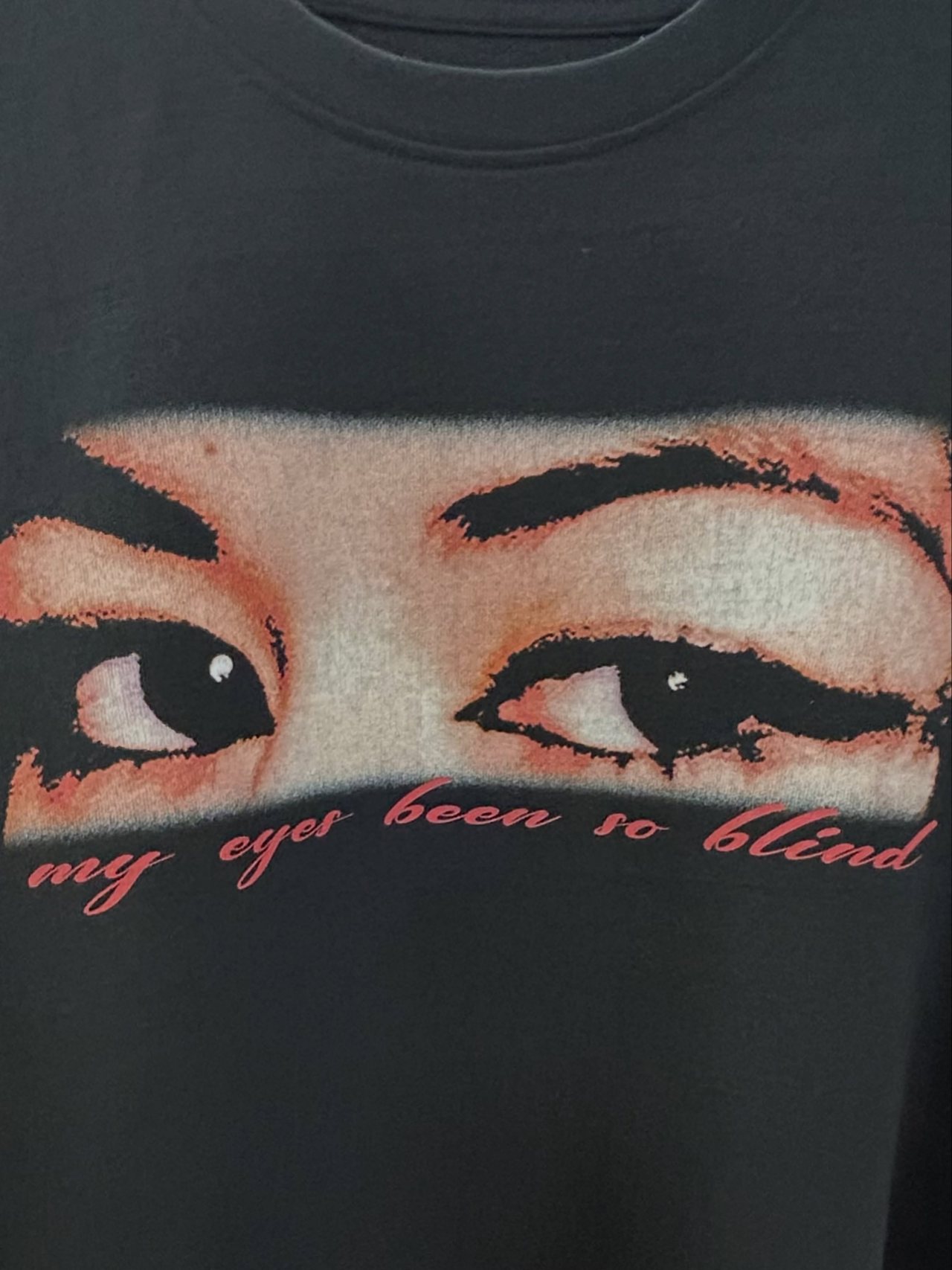 Black t-shirt printed with an eyes graphic above the words “my eyes been so blind” in red script.